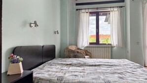 A bedroom with a bed, a chair, a window with curtains, and a radiator.