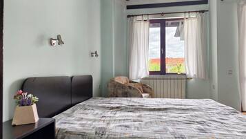 Une chambre à coucher avec un lit, une chaise, une fenêtre avec des rideaux et un radiateur.