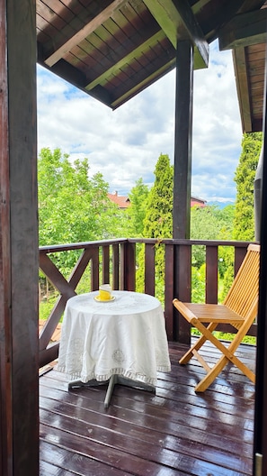 Una terrassa de fusta amb taula i cadires, amb vista a un paisatge verdós i una casa amb teulada vermella.