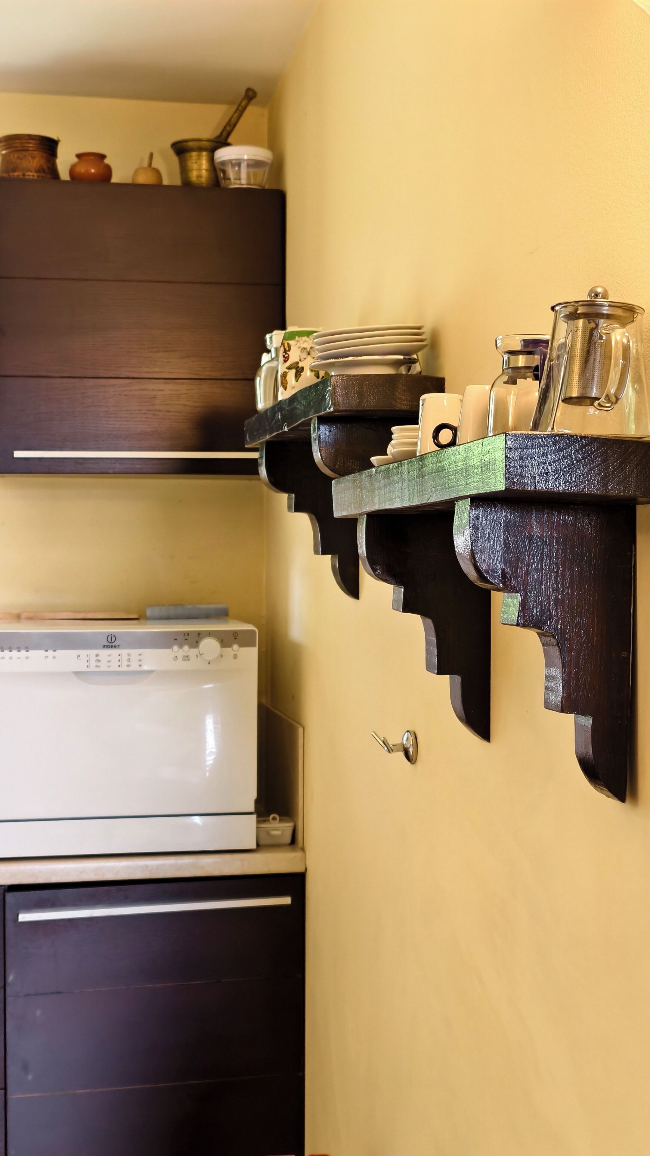 Une cuisine avec des étagères en bois où sont rangés de la vaisselle, une machine à café et un four à micro-ondes.