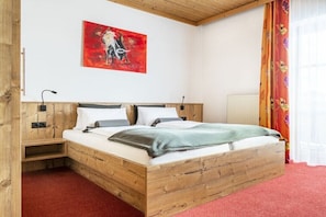 Ein hölzernes Bett mit einem roten Teppich, ein abstraktes rotes Bild an der Wand und ein Fenster mit Vorhängen.
