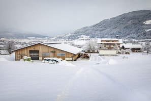 Eine verschneite ländliche Landschaft mit einem hölzernen Bauernhaus und einem weißen Gebäude.