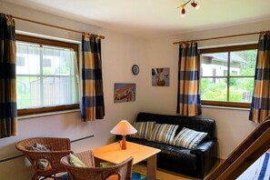 Ein gemütliches Wohnzimmer mit einer schwarzen Ledersofa, Korbstühlen, einem Holztisch mit einer Lampe und gestreiften Vorhängen.