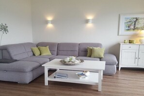 Ein Wohnzimmer mit grauem Sofa, weißem Couchtisch und einem weißen Schrank mit Lampe.