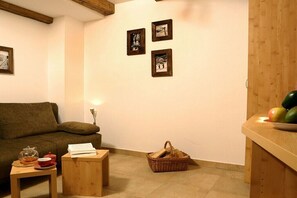 Ein gemütliches Zimmer mit einer Couch, einem kleinen Tisch mit einem Buch, einem Korb und gerahmten Bildern an der Wand.