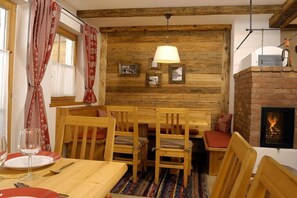 A cozy room with a wooden wall, a fireplace, a dining table with chairs, and a bench. - Chalet in Hochkrimml for 6-14 people (Krimml)