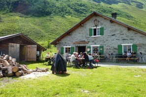 Ein Steinhaus mit grünen Fensterläden, Sitzgelegenheiten im Freien und einem Holzstapel.