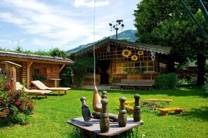 Eine rustikale Lodge mit Holzfassade, Kamin aus Stein und einem Garten mit Liegestühlen.