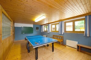 Ein Raum mit einer Tischtennisplatte, Holzbanken, einer Dartscheibe und einem Heizkörper.