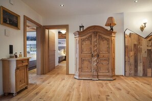 Ein Flur mit Holzboden, einem großen Holzschrank, einer kleinen Kommode und einer Tür zu einem anderen Zimmer.