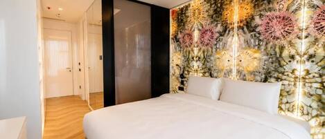 Habitación de hotel moderna con una cama grande, un muro decorativo y un pasillo que conduce a una puerta.