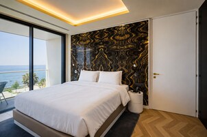 A bedroom with a large bed, a view of the ocean, a modern design with a black and gold patterned wall, and a small bedside table with a lamp.