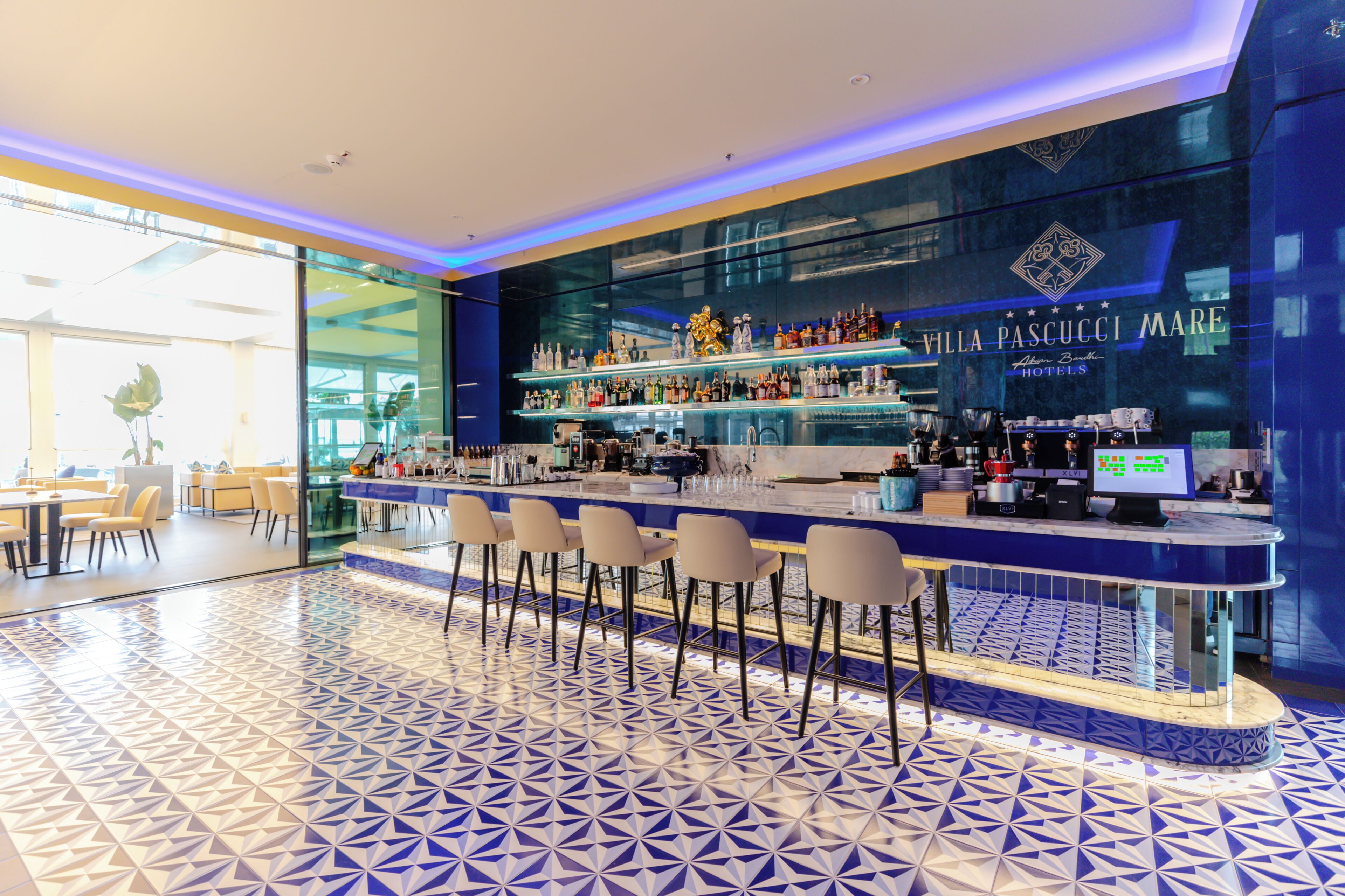 A bar area with a blue and white patterned floor, bar stools, and shelves stocked with bottles.