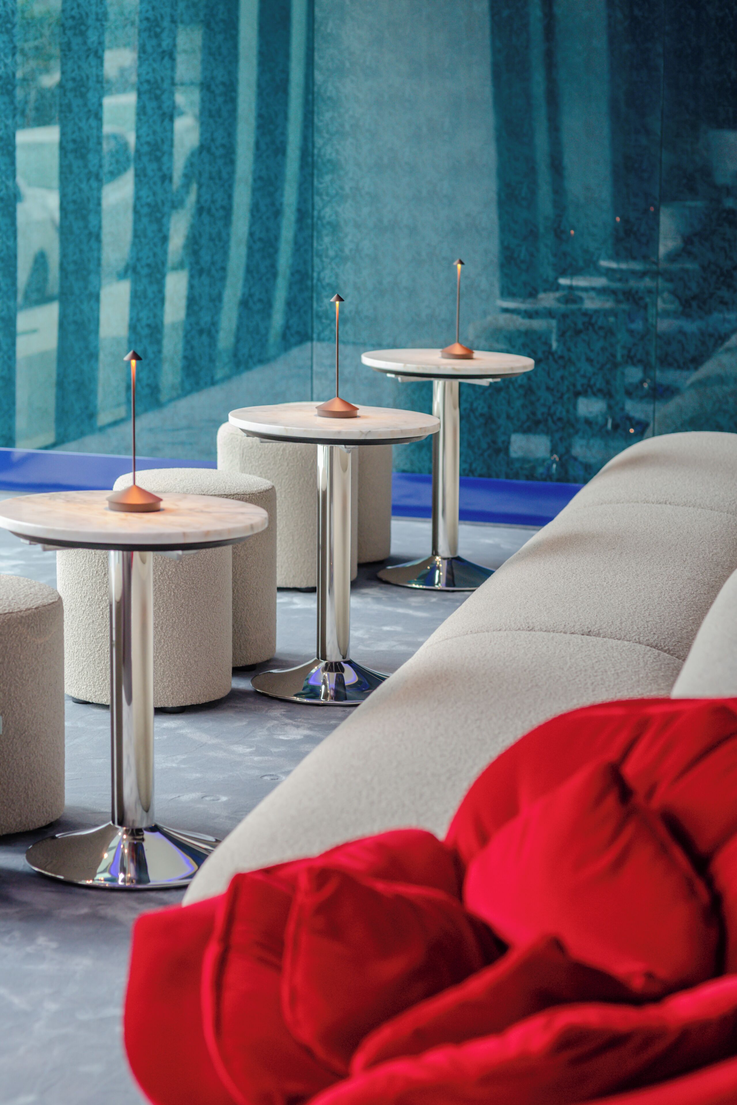 A modern interior with round tables and chairs, a red cushion, and a large window with a view.