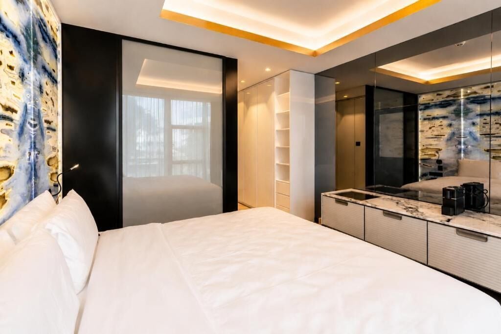 Quarto de hotel moderno com uma cama grande, armário embutido, espelho e bancada de mármore.