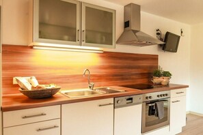 Een moderne keuken met een houten aanrecht, een roestvrijstalen spoelbak, een inbouwoven en een televisie aan de muur.