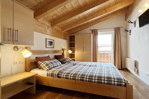 Ein Schlafzimmer aus Holz mit einem Bett, Nachttischen, einem Fenster mit Vorhängen und einem an der Wand befestigten Fernseher.