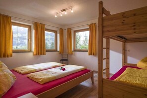 Une chambre avec deux lits, un lit superposé en bois et de grandes fenêtres avec des rideaux.