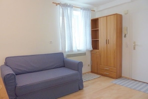A room with a blue checkered sofa, a wooden wardrobe, a window with white curtains, and a radiator.