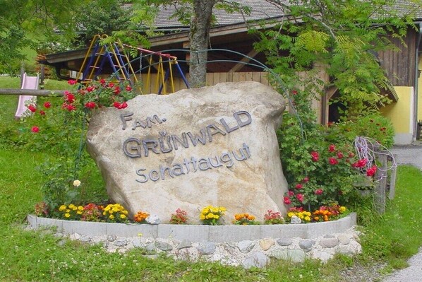 Ein Steinschild mit der eingravierten Aufschrift 'Fam. GRUNWALD Schattaugt', umgeben von einem Blumenbeet.