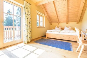 Ein Schlafzimmer mit schrägen Wänden, einem Bett, einem Fenster und Blick auf Bäume.