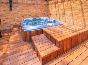Un jacuzzi con un banco de madera, frente a una pared de ladrillo.