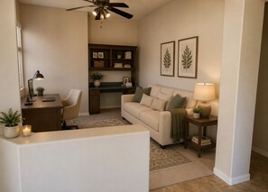 A living room with a sofa, a desk, a chair, a bookshelf, a ceiling fan, and two framed pictures on the wall. - Charming 3 bed 3 bath gated community w/ office, large chefs kitchen & laundry (Chandler)