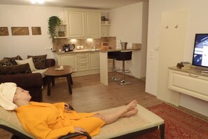 Ein Wohnzimmer mit einer Couch, einem kleinen Tisch, einer Küchenzeile und einem Fernseher.