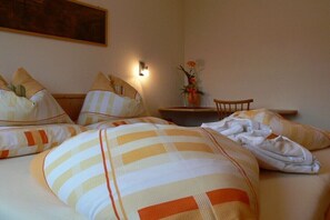 Ein Hotelzimmer mit Bett, Kissen, Nachttisch, Lampe und einer Vase mit Blumen.