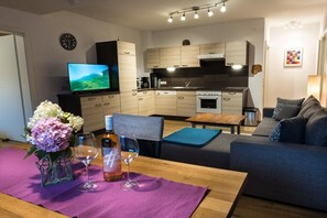 Eine moderne Küche mit Holzausstattung, einem eingebauten Ofen und einem Fernseher. Es gibt einen Essbereich mit Tisch, Stühlen und einer Couch.
