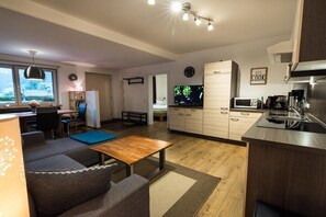 Eine moderne Küche mit Mikrowelle, Herd und Schränken, ein Essbereich mit Tisch und Stühlen sowie ein Wohnbereich mit Sofa und Fernseher.