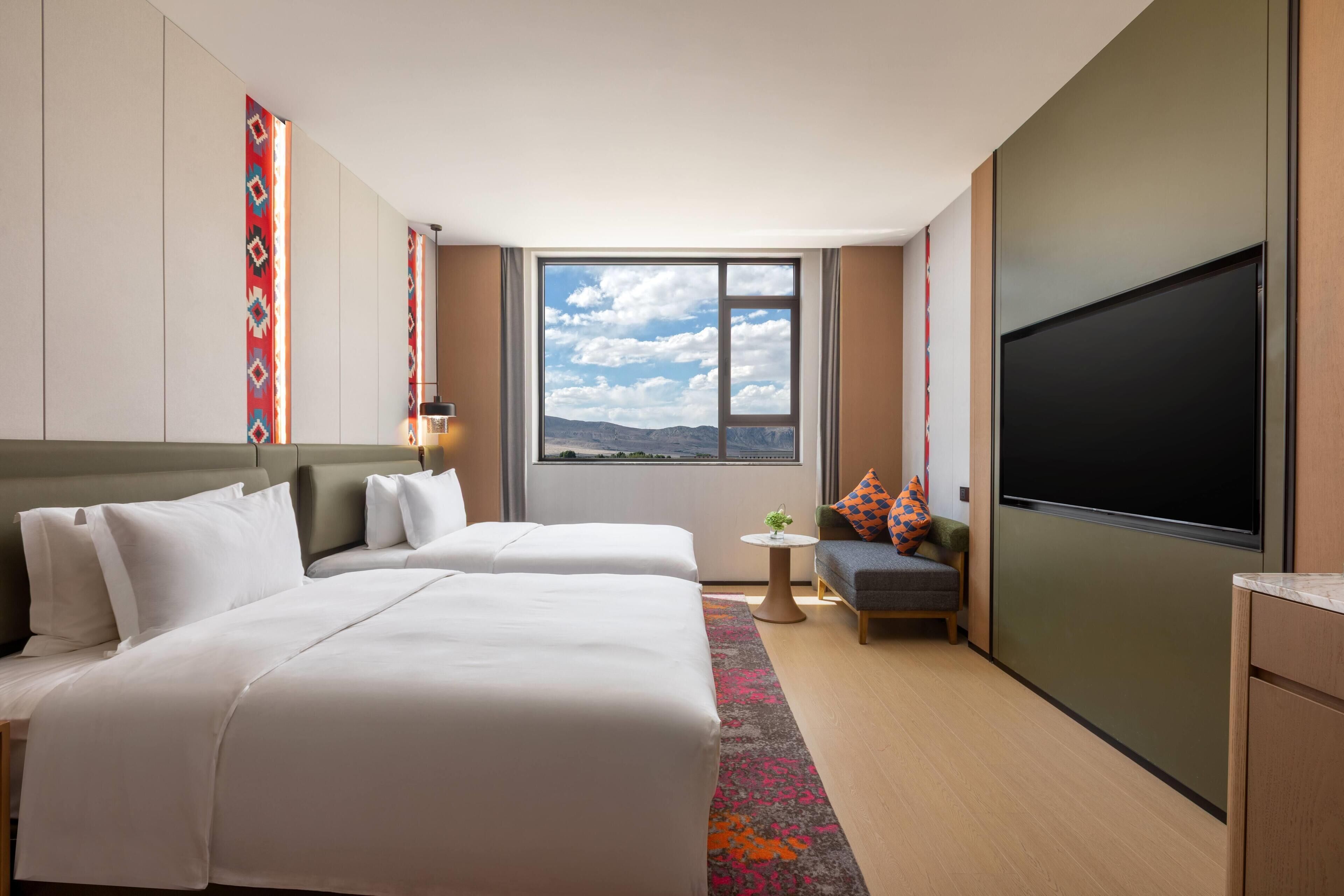 Ett hotellrum med två sängar, en TV, ett litet bord och utsikt över bergen.