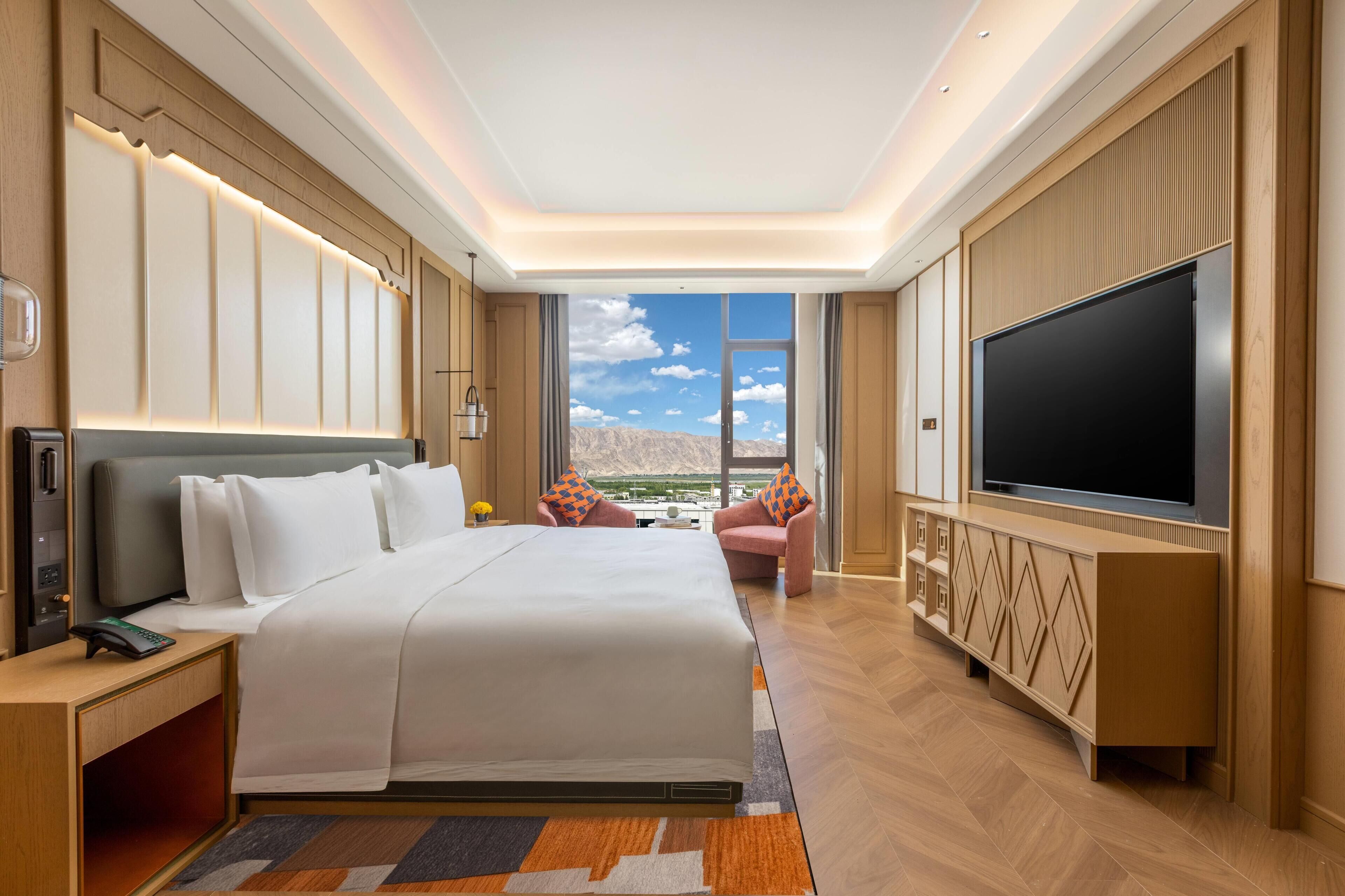 A hotel room with a large bed, a TV, a desk with a phone, and a view of the mountains.