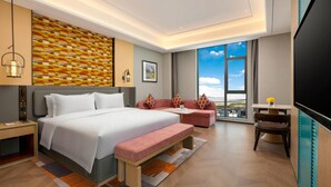 Ein modernes Hotelzimmer mit einem großen Bett, einer Couch, einer Bank, einem Schreibtisch, einem Fernseher und einem großen Fenster mit Blick auf die Stadt.