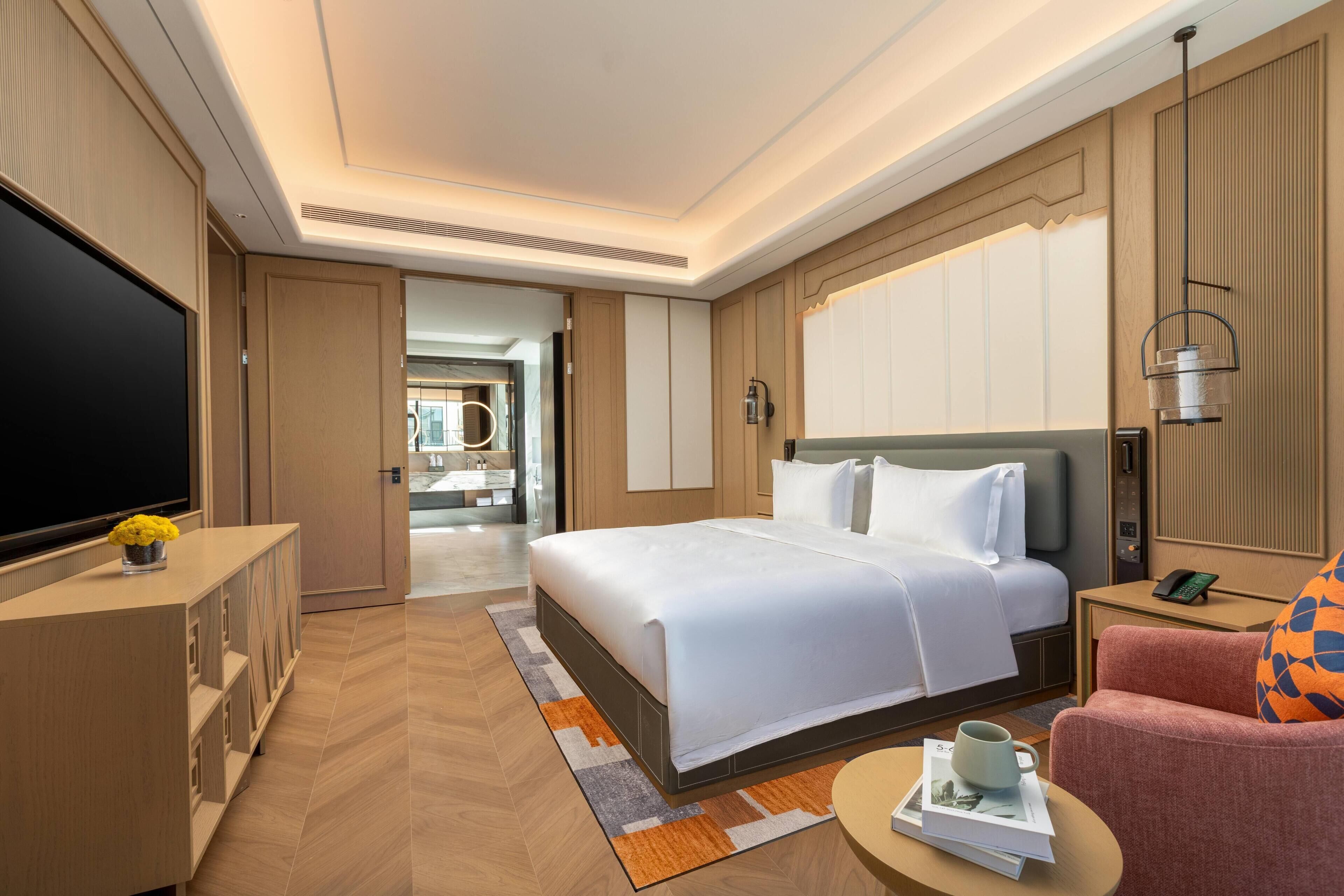 Habitación de hotel con una cama grande, un escritorio, un televisor y un baño visible a través de una puerta abierta.