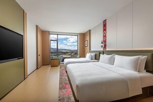 Quarto de hotel com uma cama grande, televisão, vista da cidade e parede com padrão.