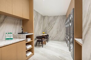 A modern bathroom with marble walls, a wooden vanity, a sink, a chair, and a row of washing machines. - Wyndham Garden Kashgar Tashkurgan (Taxkorgan Tajik)