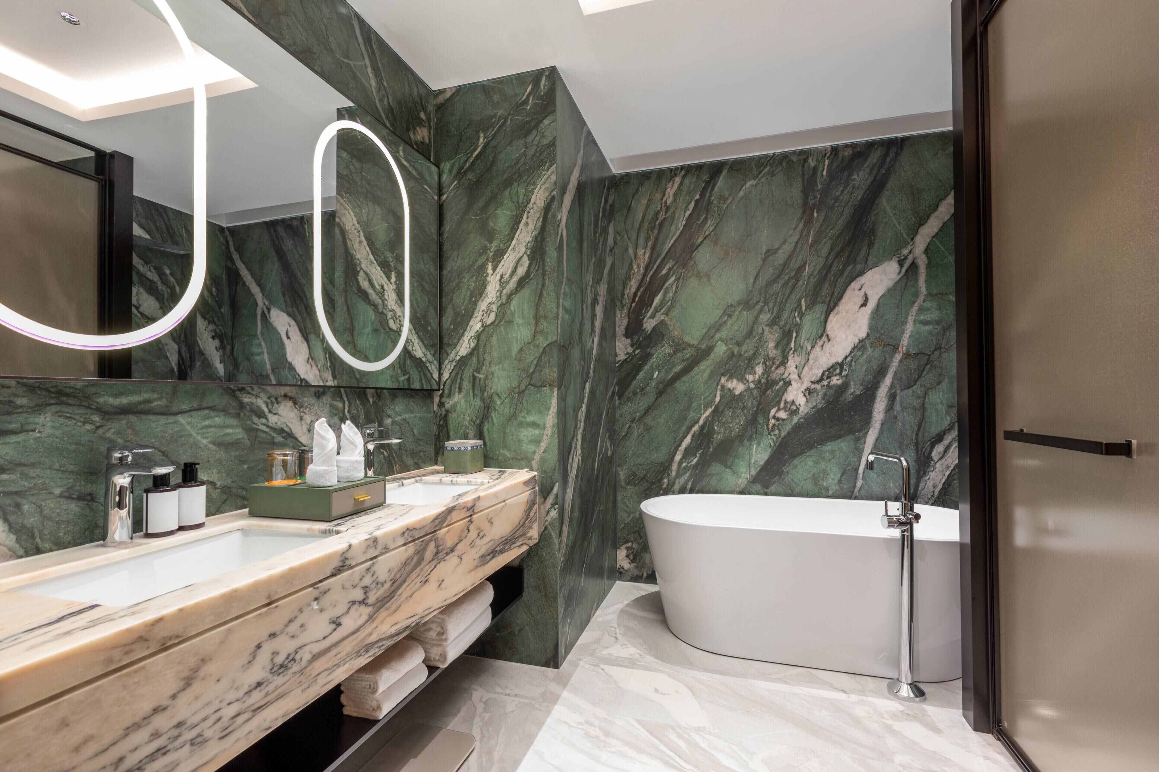 A modern bathroom with a marble vanity, a freestanding bathtub, and a large mirror with a light fixture.
