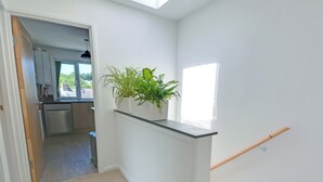 Een hal met een trap, een kamerplant en een uitzicht op een keuken.