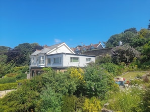 A two-story house with a bay window, surrounded by lush greenery and a garden. - 1 bedroom accommodation in Combe Martin (Combe Martin)
