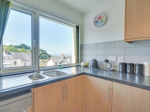 A kitchen with a window, a sink, wooden cabinets, a kettle, a coffee pot, and a clock on the wall. - 1 bedroom accommodation in Combe Martin (Combe Martin)