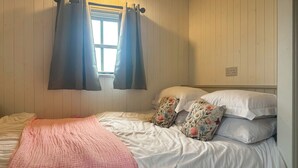 A bedroom with a bed, a window with curtains, and a bedside table. - Spring Meadow Shepherds Hut (Rowrah)