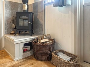 Ein Zimmer mit Kaminofen, einem Korb mit Holz und einer kleinen Ablagefläche mit Gegenständen.