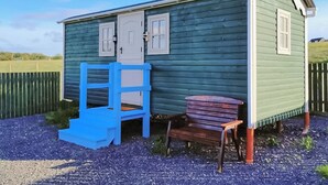 A small, single-story building with a green exterior, a white door, and a chimney. - Spring Meadow Shepherds Hut (Rowrah)