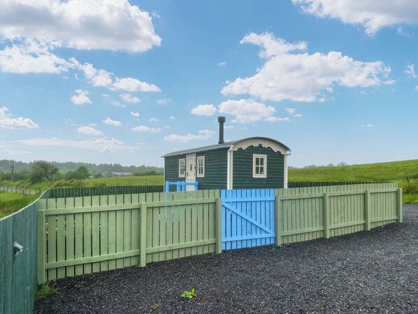 A small, single-story building with a green exterior and a blue door, surrounded by a green fence.