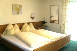 Un lit double avec du linge de lit blanc, une table de chevet avec une lampe, une petite plante en pot et un miroir au mur.