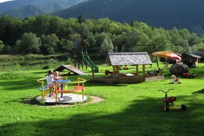 Une aire de jeux avec un toboggan, des balançoires et un petit abri.
