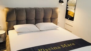 En pænt redt seng med sort sengegavl, hvide sengetæpper og et 'Piscina Mare' håndklæde for enden af sengen.
