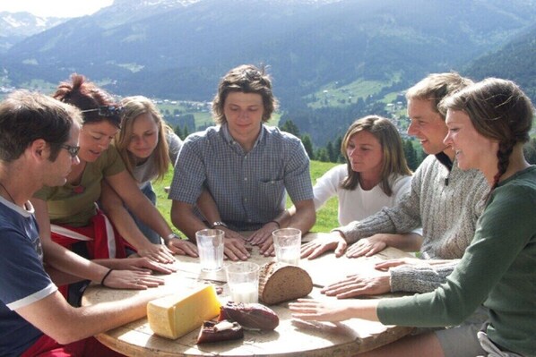 A group of people around a round table with food and drinks, outdoors with a mountainous backdrop. - Eberle Country House (Hirschegg\/Kleinwalsertal)