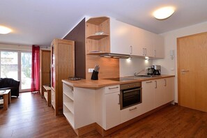 A compact kitchen with white cabinets, a wooden countertop, a built-in oven, and a window with a red curtain. - Eberle Country House (Hirschegg\/Kleinwalsertal)
